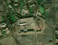 4/6 Farmyard (landuse=farmyard) composed of long buildings surrounded by a fence dotted with hay stacks, near a road very close to a village (Maxar satellite imagery).