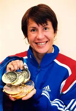 Russian cross-country skier Lyubov Yegorova in a blue and red Adidas track suit, holding her three gold medals and smiling.