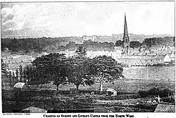 A view over trees and buildings, with a tall spire visible to right, a rectangular building in the distance.