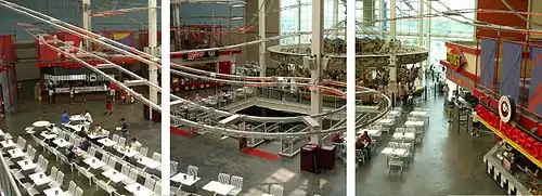 A white historic carousel in the back of a food court in a modern shopping mall