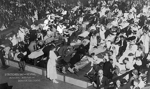 Stretcher Day at Revival in Municipal Auditorium at Denver, Colorado, 1921. The event attracted a capacity crowd of 12,000 attendees. People were carried in on cots, stretchers, chairs and beds; and awaited McPherson to pray over them for healing.