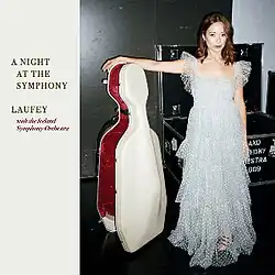 Laufey standing backstage at the concert wearing a long silver dress with her right arm resting on a cello case looking towards the viewer, the album title appears on the left on a white background