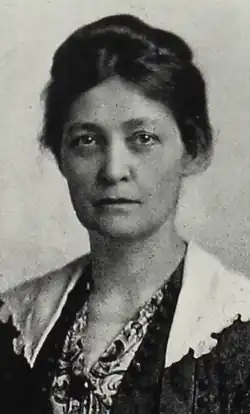 A white woman with dark hair in an updo, wearing a print blouse and a dark jacket with white lace lapels