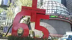 A giant sculpture that reads "Plus 65". The plus symbol has the phrase With one voice, rescue now! inscribed.