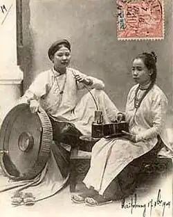 Two women wear áo ngũ thân, the predecessor of the áo dài worn in the 19th and early 20th centuries depicted on the postcard.