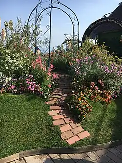 A grassy area with a metal arch surrounded by plants and a narrow paved brick path at the Nunobiki Herb Garden in Kobe, Japan.