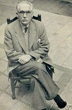 An ageing man in a formal suit, with white receding hair and a full moustache.