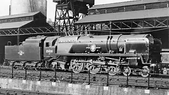 A posed side-and-front view of the rebuilt form of the locomotive, standing in the sidings of a locomotive depot. The locomotive is of conventional appearance, with a visible boiler and no flat covering plates. Smoke deflectors are fitted at the front of the locomotive.
