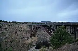 A dusk picture of a steel arch bridge spanning a deep canyon. In the background the corner of a 2nd bridge is visible.