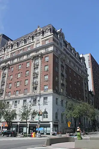 View of the Marseilles from the intersection of Broadway and 103th Street. The facade is largely made of red brick, except at the base, where it is made of stone. The top of the hotel contains windows within a black mansard roof.