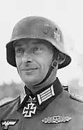 Black-and-white portrait of a man wearing a steel helmet, military uniform with an Iron Cross displayed at his neck.