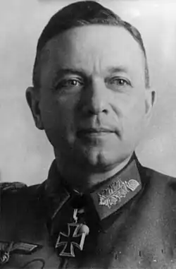 The head of a man, shown in semi-profile. He wears a military uniform with a military decoration in shape of an iron cross displayed at the front of his shirt collar. His hair is dark and combed to back.