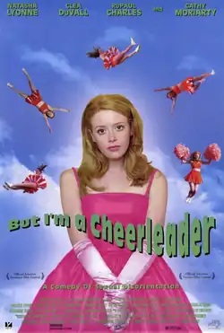 A half-length portrait of a teenage girl with long hair, wearing a bright pink formal dress and satin gloves. At a distance over her head five cheerleaders in orange outfits perform, flying through the sky. Across the portrait reads, "But I'm a Cheerleader", and below, in smaller letters, "A Comedy of Sexual Disorientation".