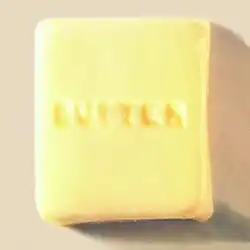 A photograph of a square of butter with the word "butter" carved into it in all caps.