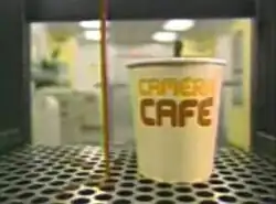 An image of a paper cup, inside a coffee machine. The series title is displayed on the cup.