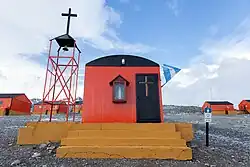 a small one story orange building on yellow steps with a cross and bell tower on its side.