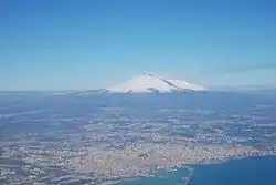 An aerial view of the metropolitan city around Catania. Mount Etna is the peak at a distance.