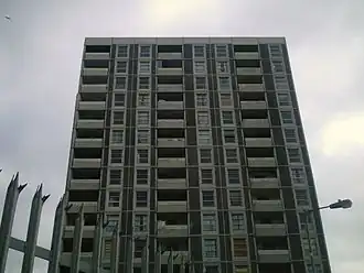Eleven storeys of a gray residential tower, with a spiked fence and a lamp in the foreground.