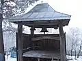 A fixed wooden semantron beneath bells at Căpuşneni church, Romania