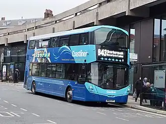 Two-tone blue double-decker bus at a city centre bus stop, destination reading '843 to Scarborough, departs in 4 minutes'