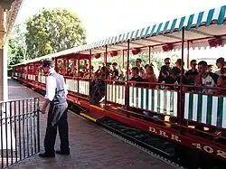 A series of red-colored gondola train cars with green-and-white-striped awnings. A train conductor is in the foreground.