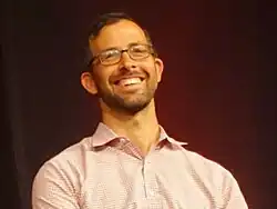 Person with glasses in front of a dark background
