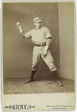 A sepia-toned baseball card image of a man in old-style white baseball pants, jersey, and cap pantomiming throwing a baseball with his right hand