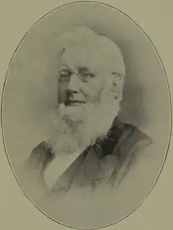 An elderly man with a white beard and glasses, wearing a suit, depicted in an oval-shaped vintage photograph.