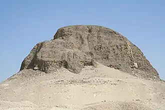 Pyramid sitting on a rocky outcropping. Large portions of the pyramid are missing.
