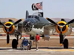 Closeup of bomber on tarmac with two older men, one in a wheelchair looking on