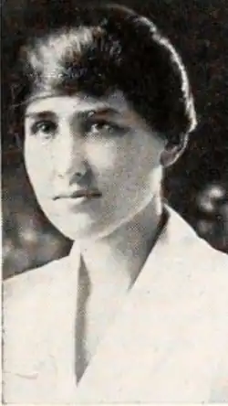 A young white woman with dark hair and eyes, wearing a white blouse