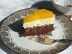 A slice of Fanta cake served on a decorated plate. It is a three-layered sponge cake, where the top layer is made from Fanta.