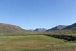 View of interior Fljót showing a grassy field and mountains on either side in the distance
