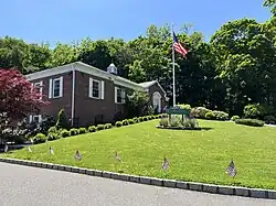 Flower Hill Village Hall in 2023, with flags on the lawn to celebrate Memorial Day