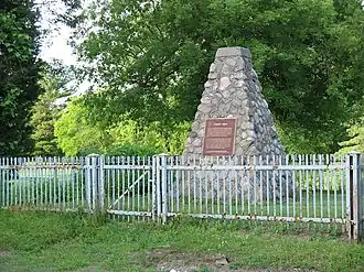 Stone cairn with plaque affixed behind a steel picket fence