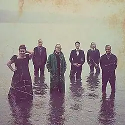 A photo of the six band members stood in knee-high water.