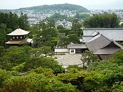 Trees and a raked sand garden next to traditional Japanese buildings.