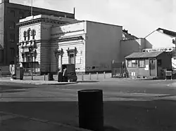 One small wing of the previously-illustrated building, with temporary huts in the place of the rest of the structure.