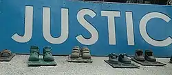 Several bronze sculptures of toddlers's shoes. The phrase "justice" is written in Spanish.