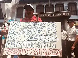 Guatemalan man in front of Constitutional Court holding sign that says "no queremos el saque do los recursos de Guatemala fuera toda minera"