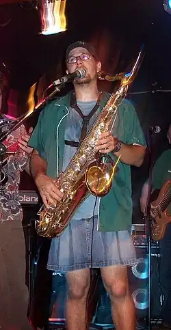 A man in a band, wearing a skirt and playing a saxophone, 2005