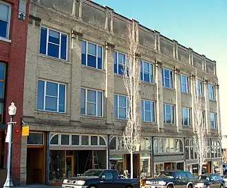 A historic white brick building with cars parked on the street in the foreground
