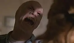 A mutant human with black eyes, sharp fangs, and no ears prepares to attack a woman.