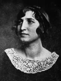 A white woman with dark bobbed hair, wearing a dark top with a white lace collar