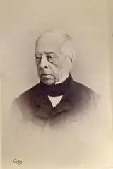 Sepia head and shoulders of older man, fair skin and hair, balding, wearing mid-19th century business suit, with a black stock tie