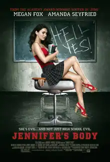 Jennifer holding books in her arms sitting on a school desk, wearing a red top and short plaid skirt, in front of a blackboard with the words HELL YES! written in chalk. A hand can be seen trapped by the lid of the school desk. The poster bears the tagline "She's evil ... and not just high school evil" in white block capital letters, with the film title underneath in large red block capital letters.