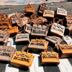 A pile of handbags on a crosswalk with "delusional" spray-painted on them, sometimes misspelled.
