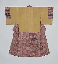 A man's underkimono viewed from the back. It has short sleeves sewn to the body for most of their length. The underkimono is made of a light yellow fabric with fine beige stripes, and the hems and collar are made from two different kinds of arabesque fabric on brick red and darker red.