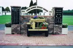 Front end of a jeep, sticking out of brick wall with plaques on brick pillars either side