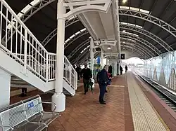 Train station island platform with a large shelter above and a ramp and stairs to access the platform